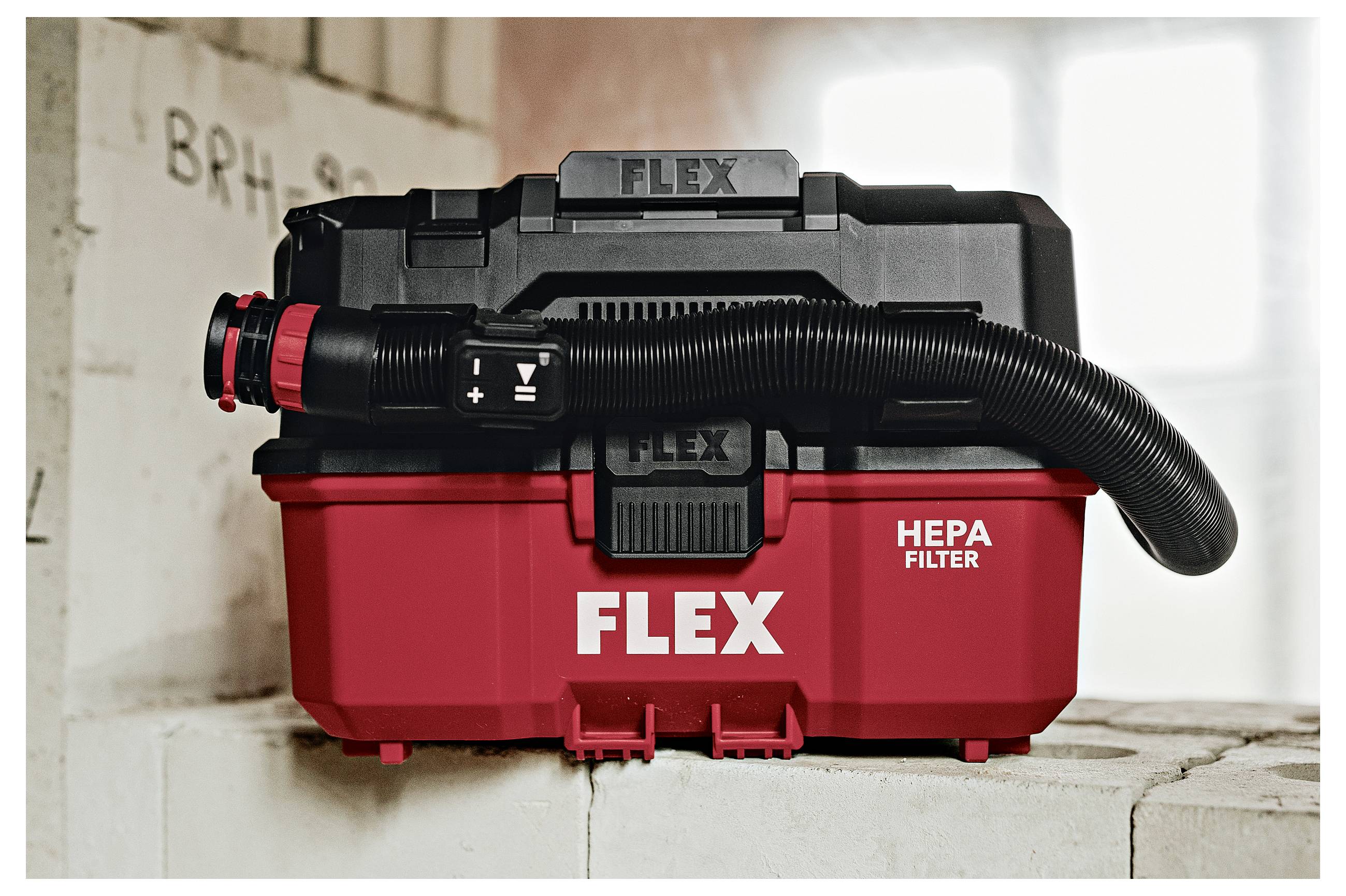 Rode FLEX HEPA-filter nat/droge stofzuiger met zwarte slang op een betonblok binnenshuis.