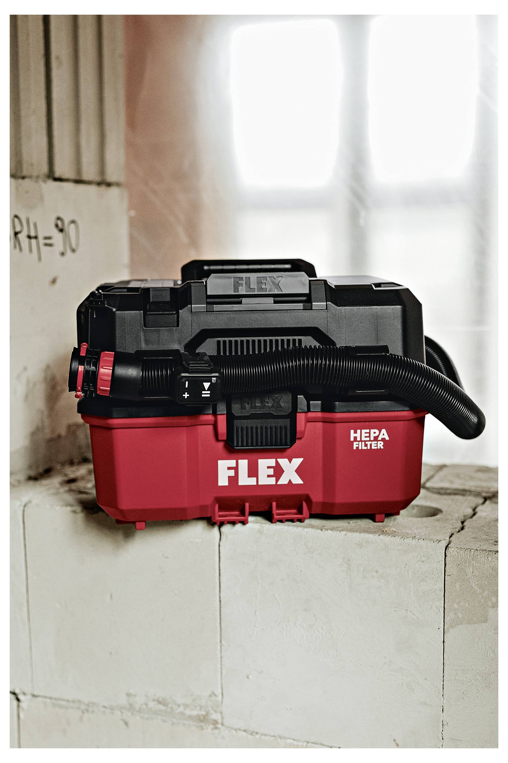 Rood-zwarte FLEX HEPA-filterstofzuiger, weergegeven op een betonblok in een werkplaats- of bouwomgeving.