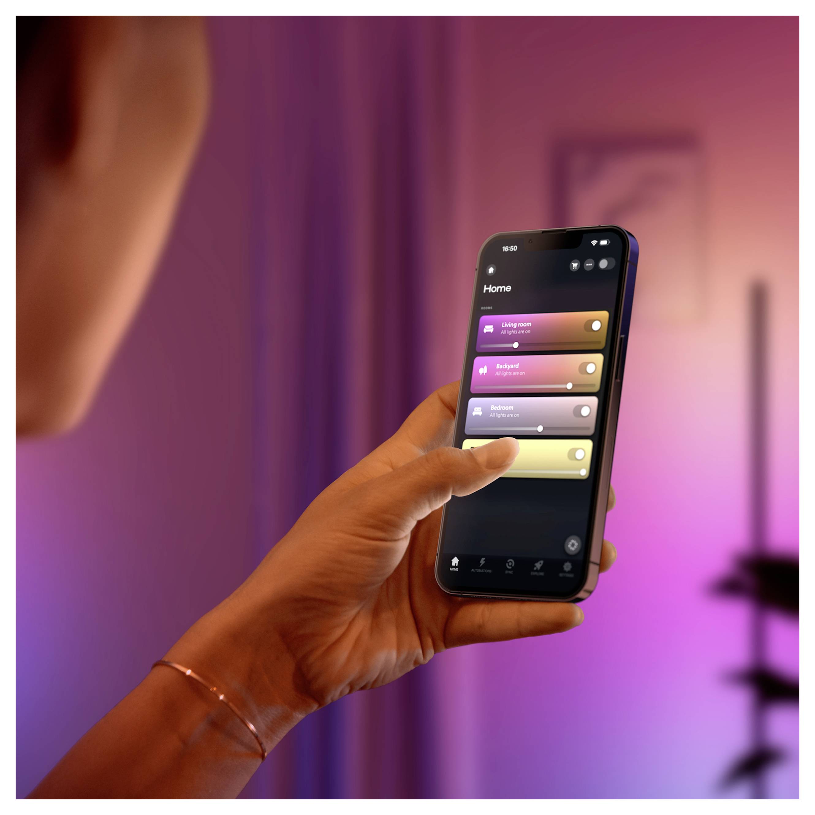Persoon die een smartphone vasthoudt met een smart-home-besturingsapp met verlichtings- en kamerbesturingen op het startscherm.