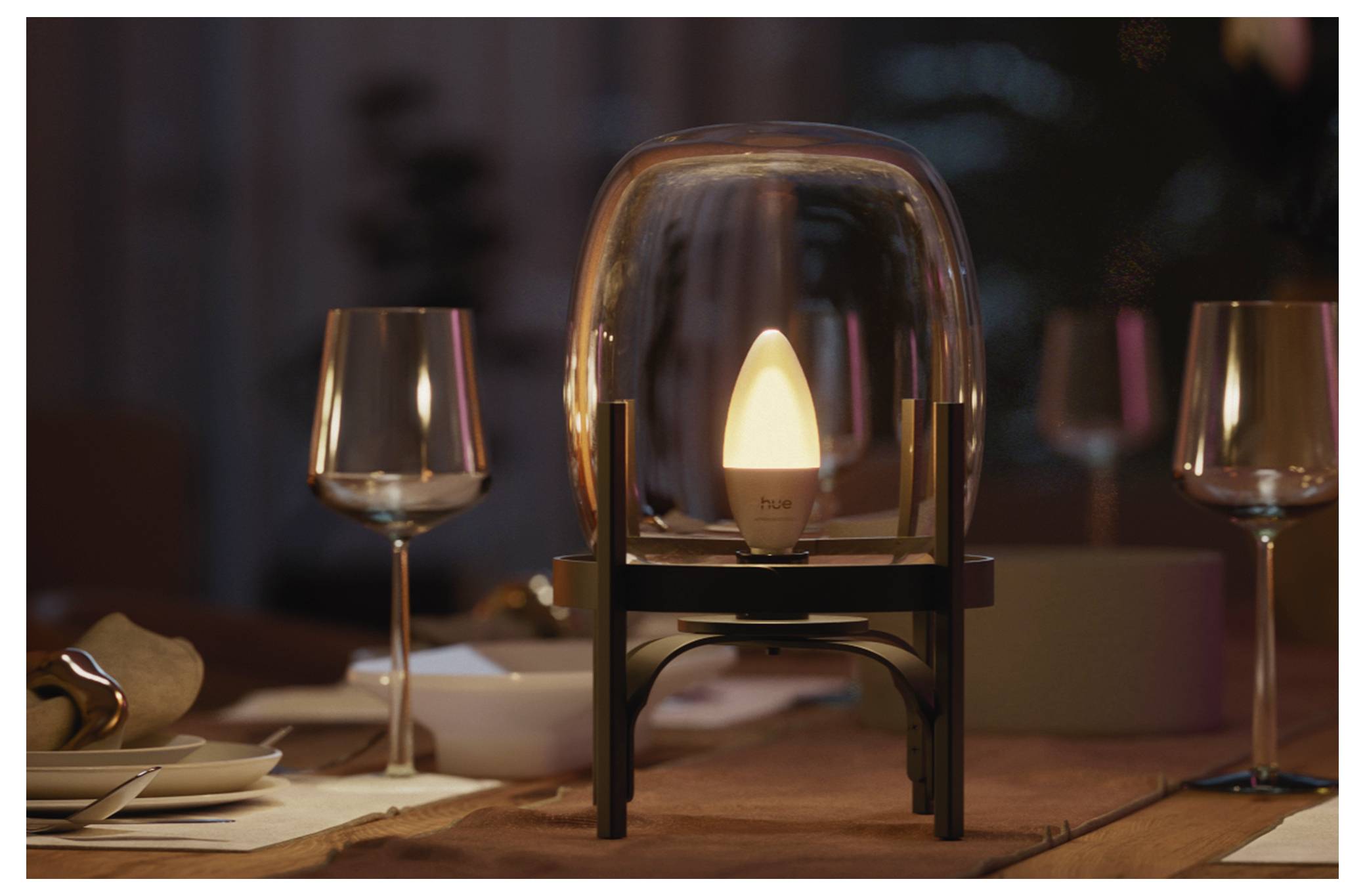 Een gloeiendo tafellamp onder een heldere glazen koepel staat op een gedekte eettafel met wijnglazen en borden, wat een warme dineerbiance creëert.