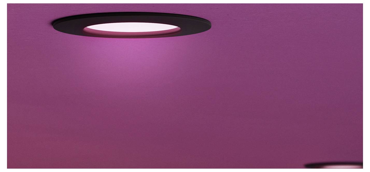 Roze plafond of muur met twee circulaire inbouwspots, één groot licht linksboven en een gedeeltelijk zichtbaar licht rechtsonder.