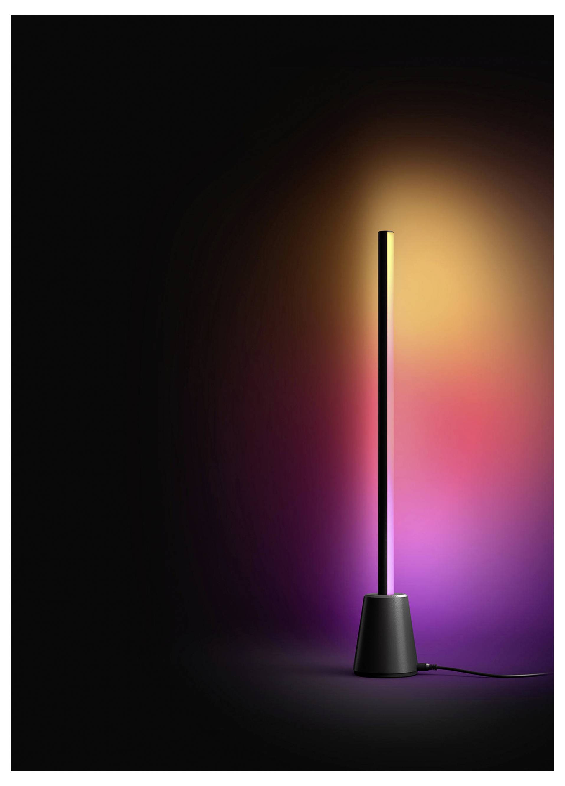 Hoge zwarte LED-lamp op een donkere achtergrond, die een warm geel-tot-roze gloed erachter werpt, met een zichtbaar stroomsnoer aan de basis.