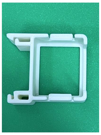 Wit plastic bevestigingsframe of clip op een groene getextureerde achtergrond, weergegeven in close-up.