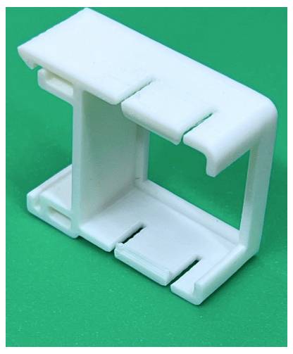 Witte kunststof clip of beugel met een open rechthoekig frame, weergegeven op een groene achtergrond.