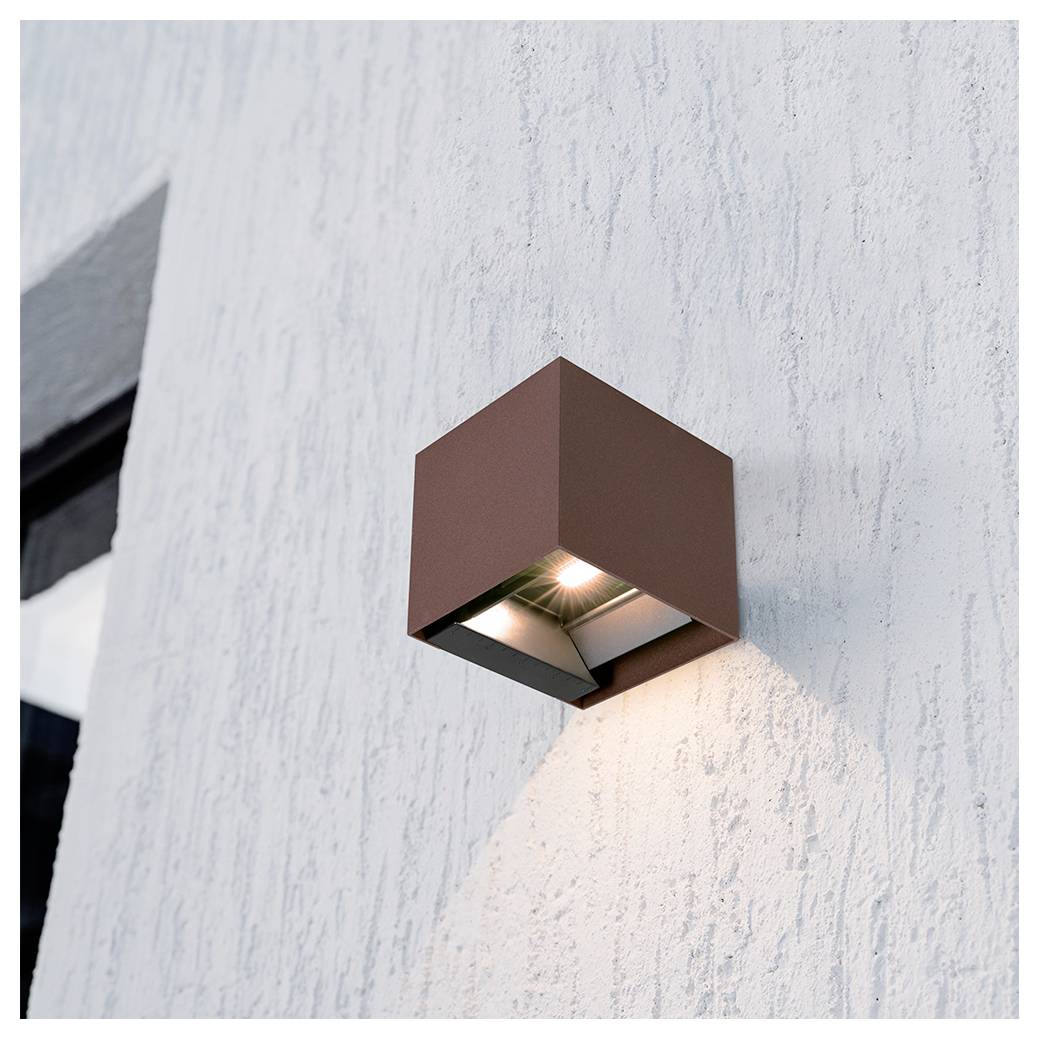 Modern bruin kubisch wandlicht geïllumineerd op een witte gestructureerde buitenmuur, dat een zachte neerwaartse gloed uitstraalt.