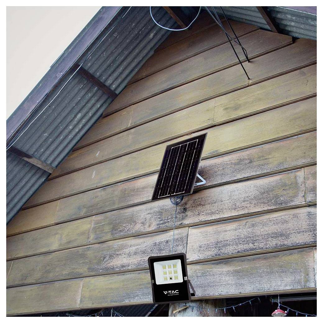 Klein zonnepaneel op een houten muur gemonteerd voorziet een VTAC LED-schijnwerper van stroom die onder een golfmetalen dak hangt.