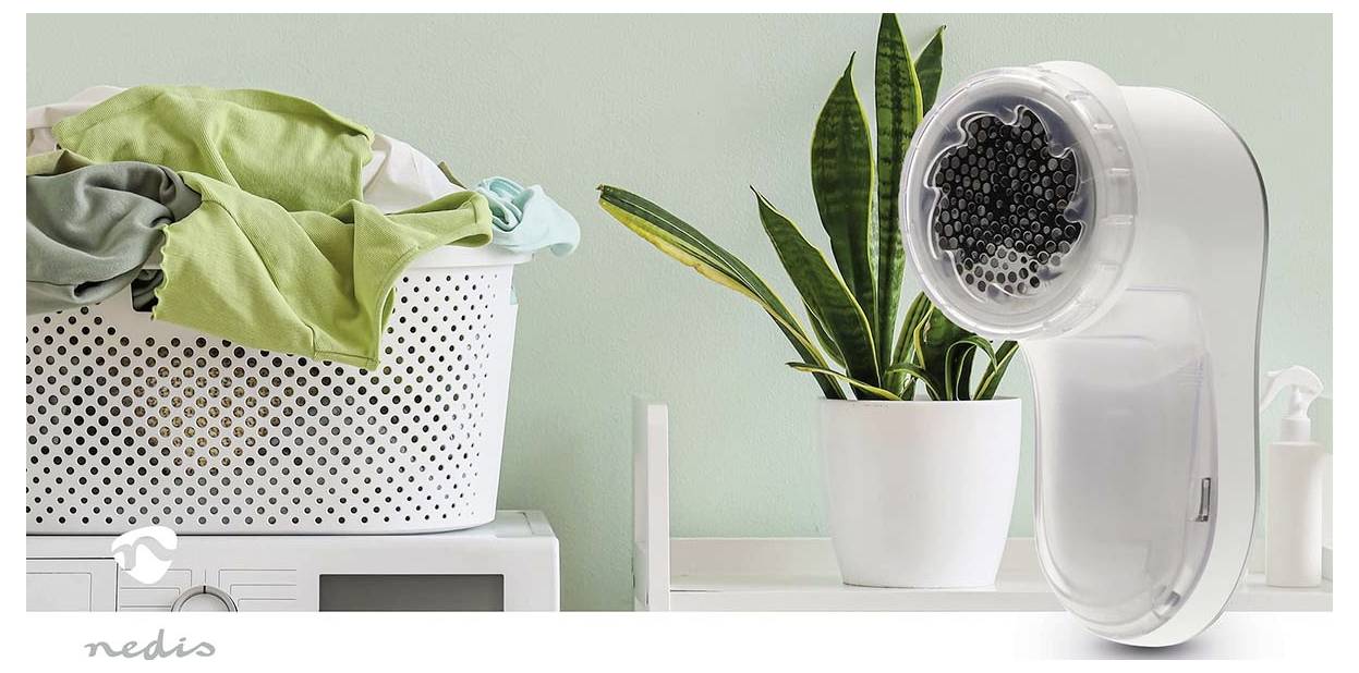 Draagbare elektrische kledingdroger met een transparante trommel naast een potplant en een wasmandje gevuld met kleding.