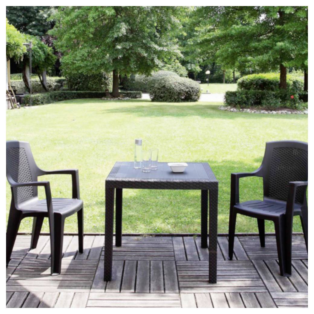 Twee lege stoelen staan tegenover elkaar aan een klein tafeltje op een houten terras met uitzicht op een zonnige, aangelegde tuin.