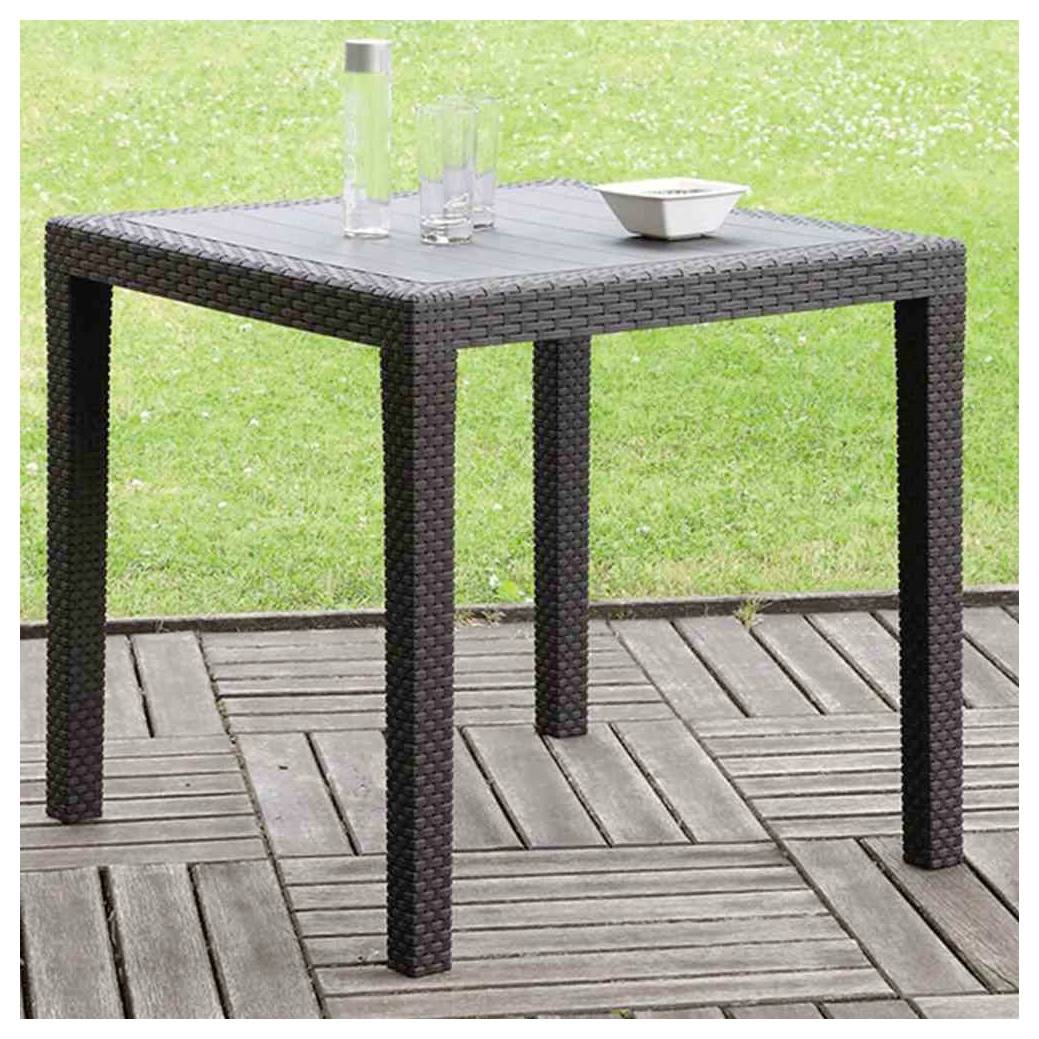 Vierkante patiatafel in rattan-stijl voor buiten met glazen blad, met een karaf, glazen en een kleine schaal op een houten terras naast gras.