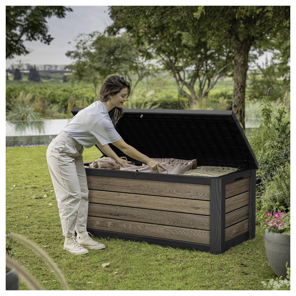 Vrouw die items in een grote buitenopslagbox in een grazig tuingebied in de buurt van een vijver verpakt.