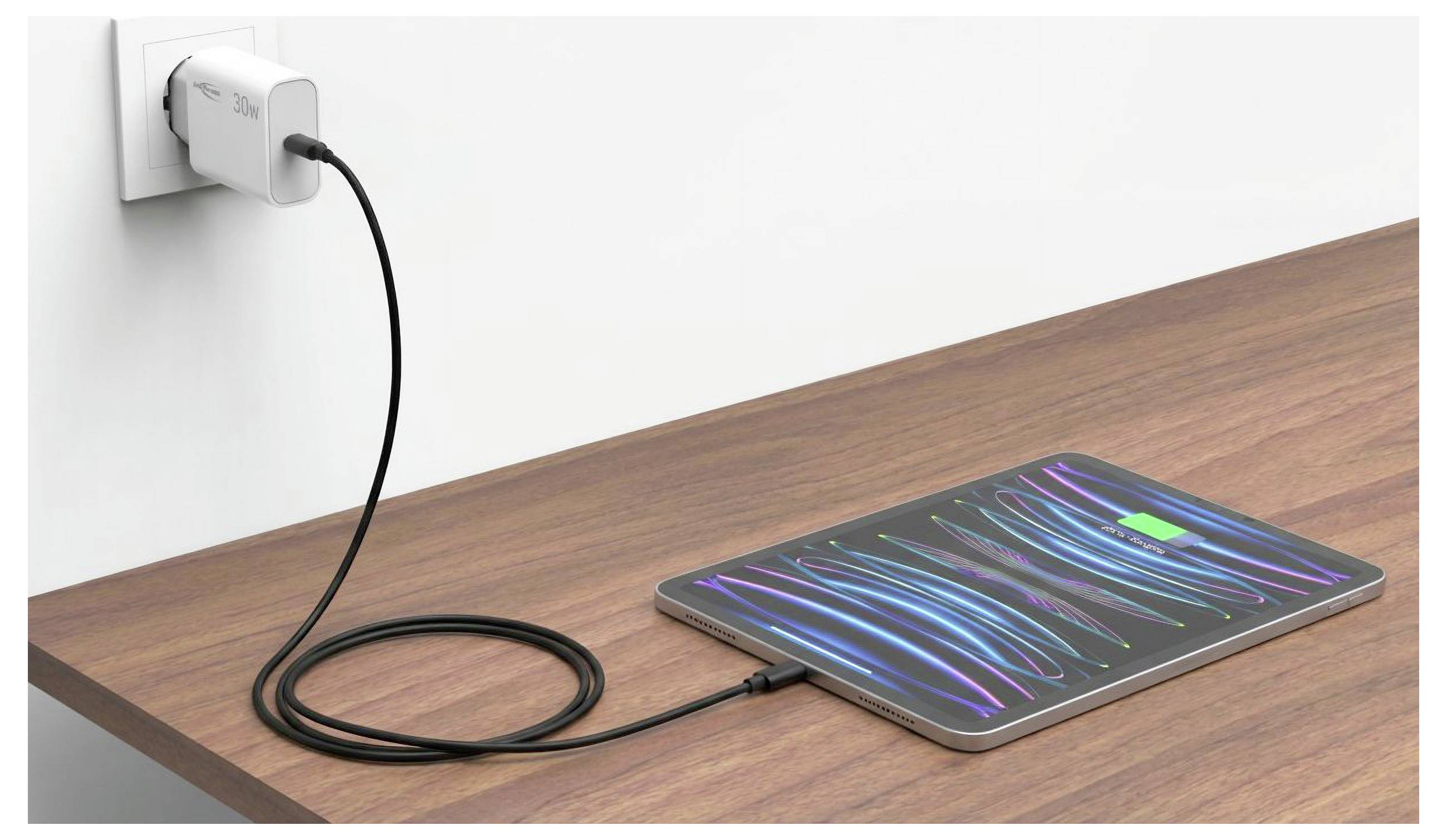 Tablet die oplaadt op een houten bureau, verbonden via een kabel met een wandcontactdoos en met een kleurrijk abstract scherm.