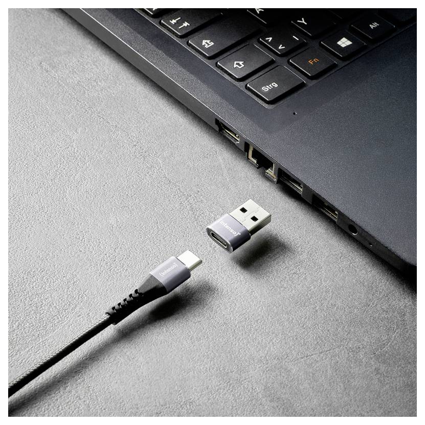 USB-C-kabel met afneembare USB-A-adapter naast de USB-poorten van een laptop op een grijs oppervlak.