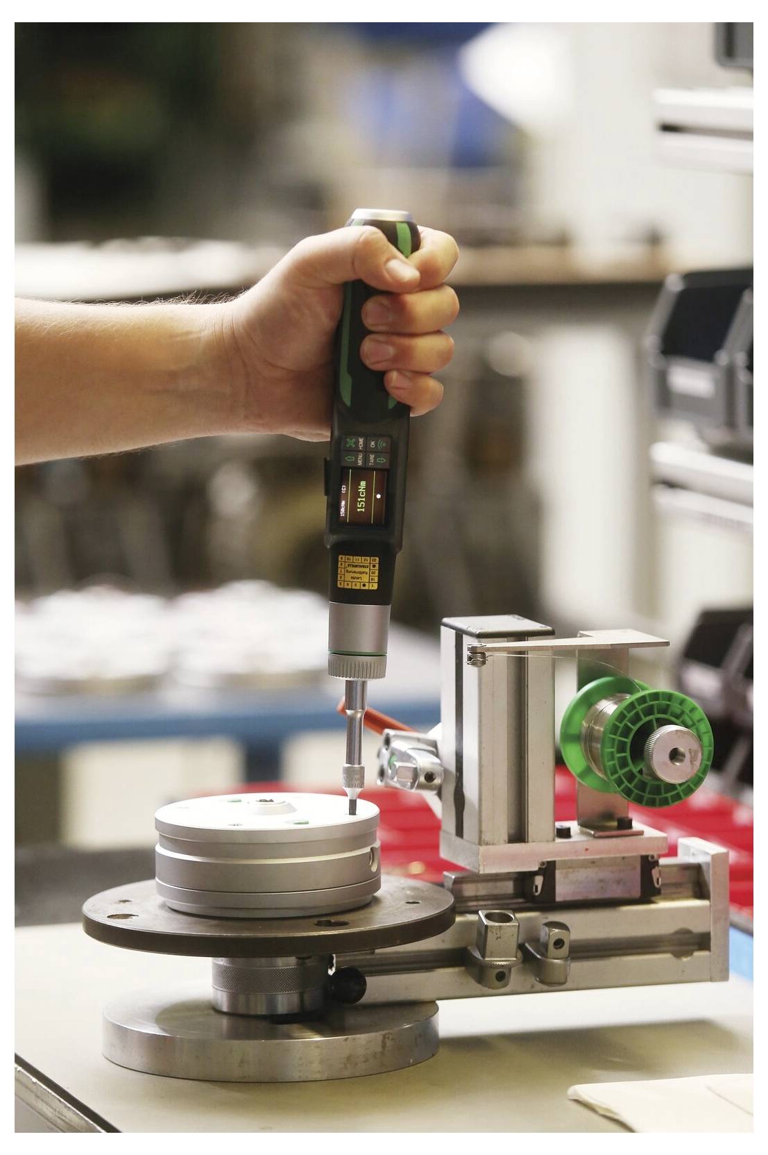 Een persoon gebruikt een handheld elektrische schroevendraaier op een kleine machine-inrichting in een werkplaats, wat duidt op assemblage- of nauwkeurig reparatiewerk.