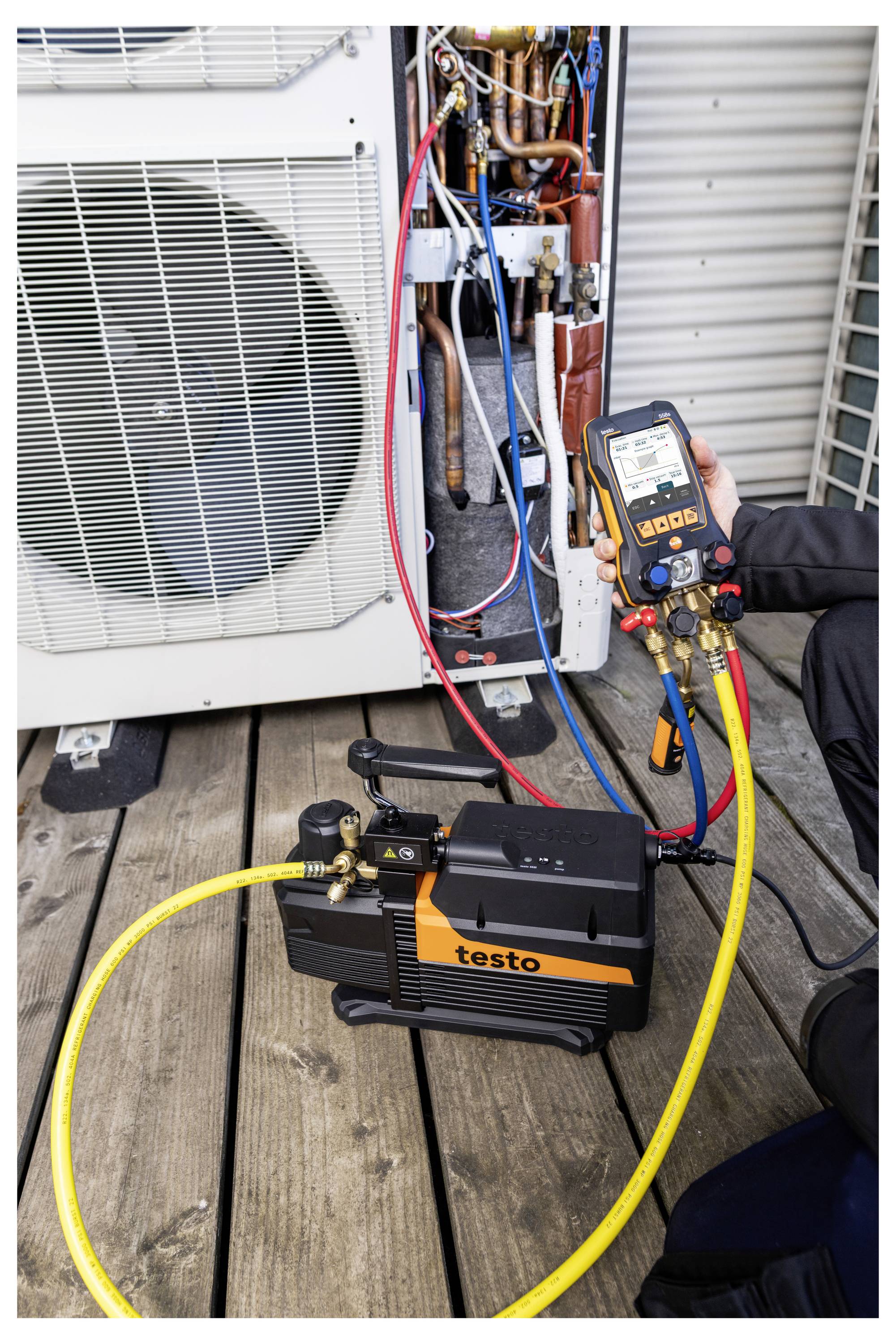 Technicus die een buitenairconditioner test met een Testo-manometer en slangen die op de blootgestelde koudemiddelleidingen van de unit zijn aangesloten.