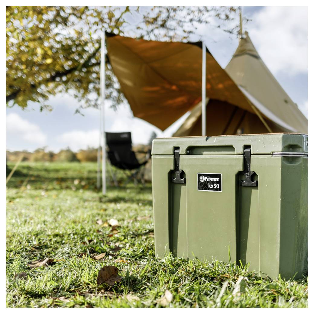 Groen hard case gelabeld 'Permix ko50' op gras voor een campingtent met een oranje luifel buiten.
