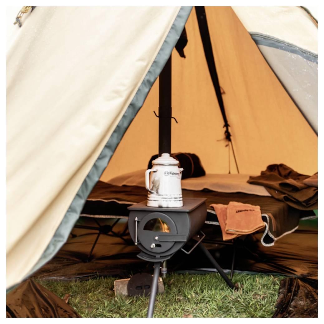 Kampeerbrander binnen in een tent, met een ketel erop en een slaapopstelling op de achtergrond.