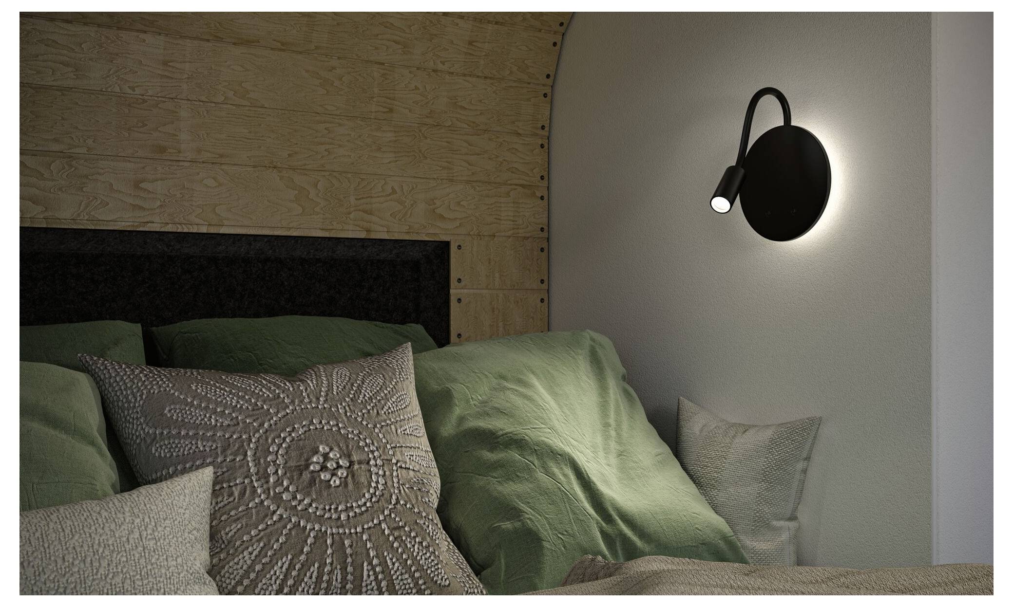 Een slaapkamerbed met groen beddengoed en gemusterde kussens, verlicht door een zwarte aan de muur bevestigde leeslamp aan de rechterkant.