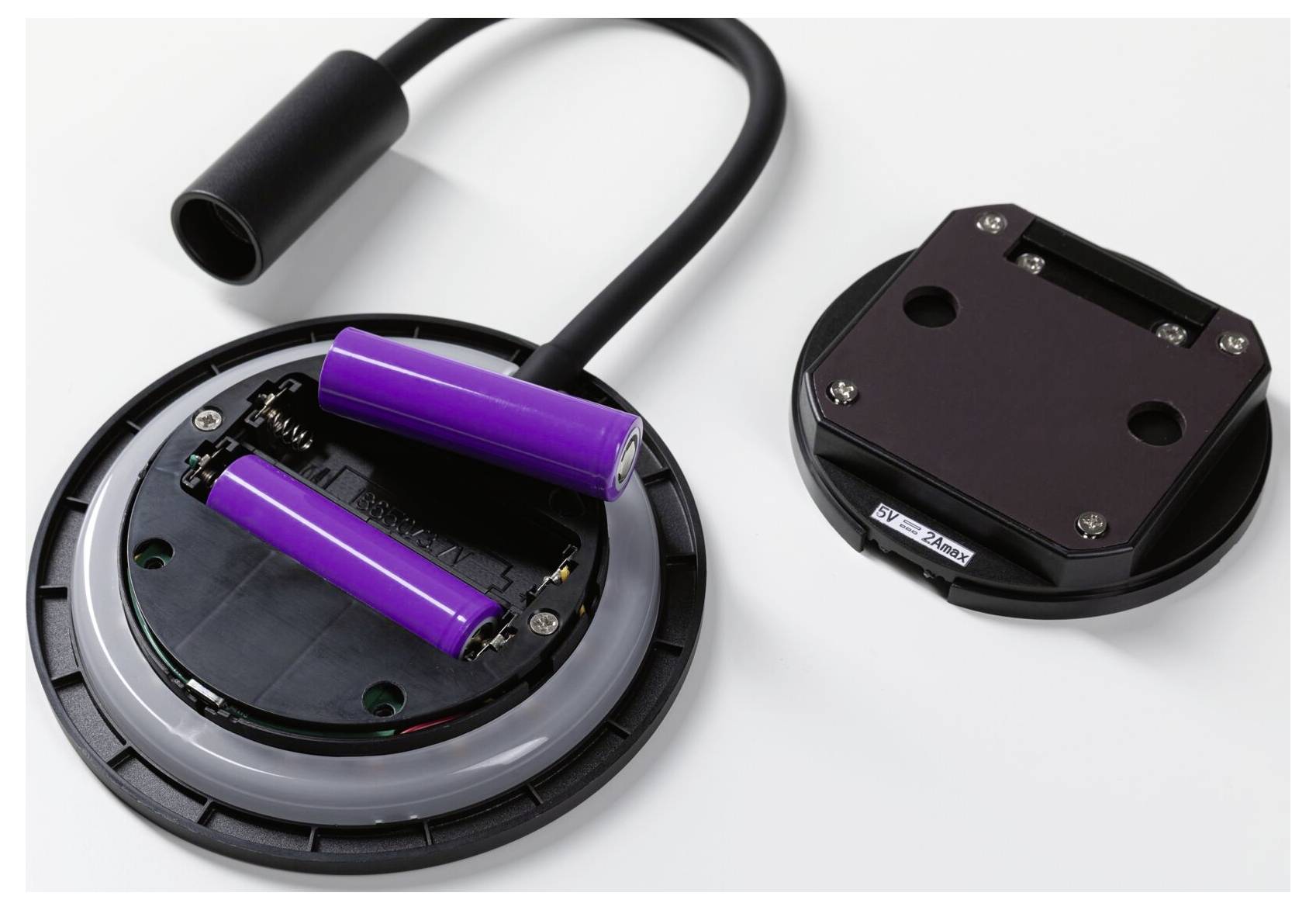 Open batterijvak met twee paarse oplaadbare batterijen en een losgemaakt zwart deksel op een witte achtergrond.