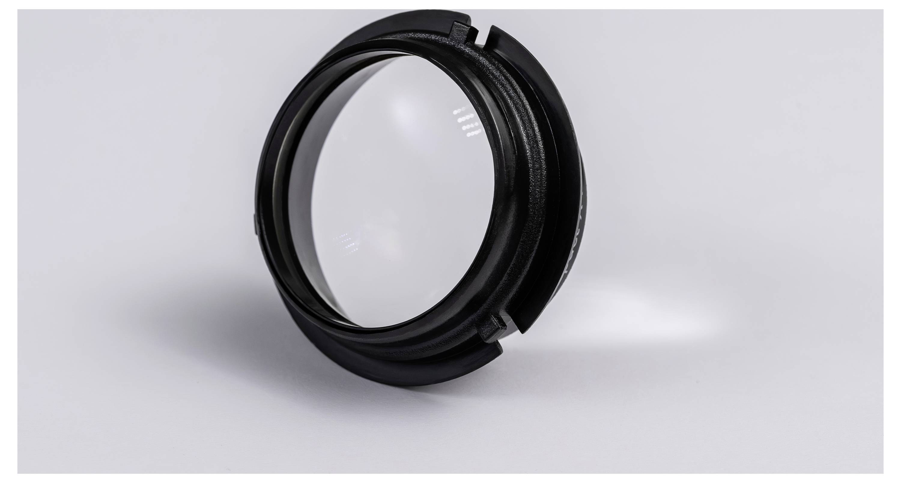 Een zwart cirkelvormig cameralensfilter of adapterring die rechtop op een lichtgrijs oppervlak staat.
