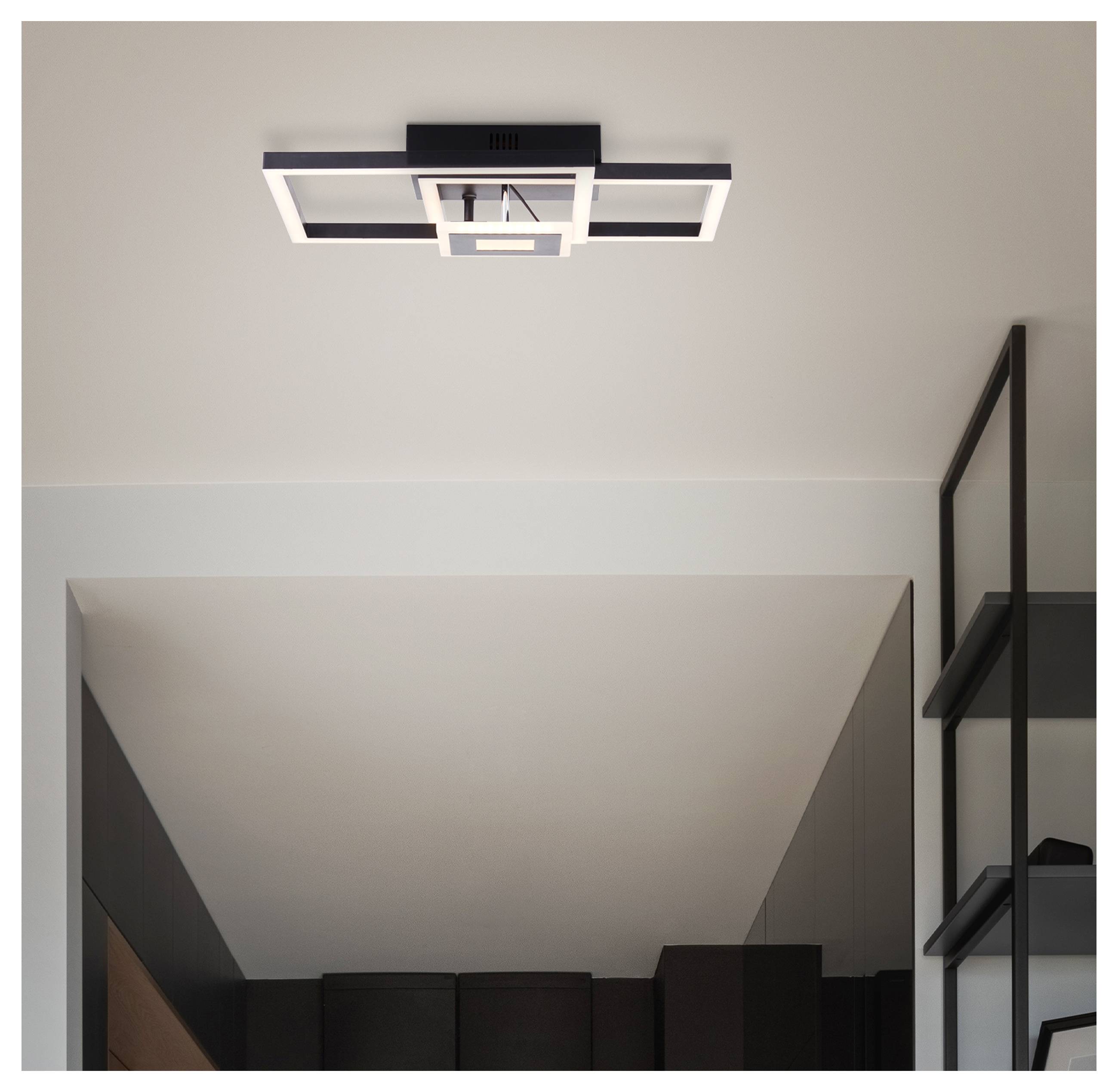Modern geometrische plafondlamp gecentreerd op een wit plafond, met donkere planken zichtbaar langs de rechterkant van een kamer.