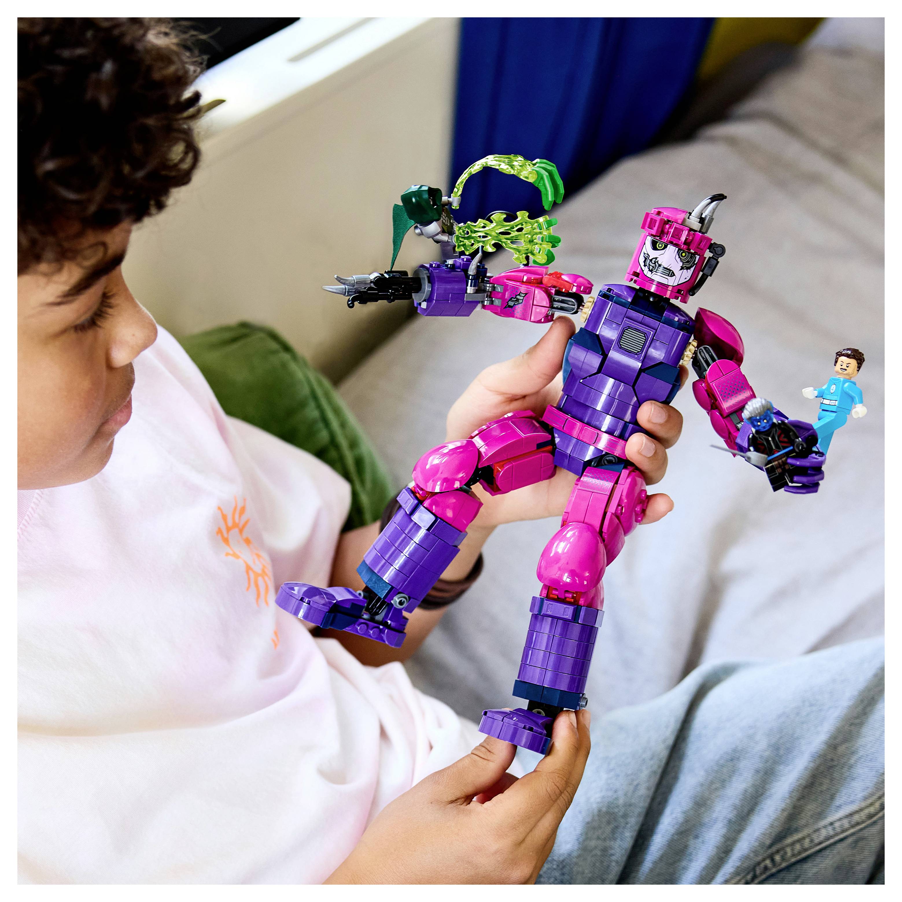 Kind dat een kleurrijke paars en roze robottenspeelgoed met een klein actiefiguur vasthoudt, zittend op een bed of bank.