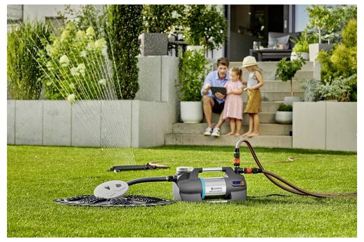 Draagbare elektrische hogedrukspuiter op een gazon die water spuit om een patio schoon te maken terwijl een man en twee kinderen toekijken vanaf de trappen.