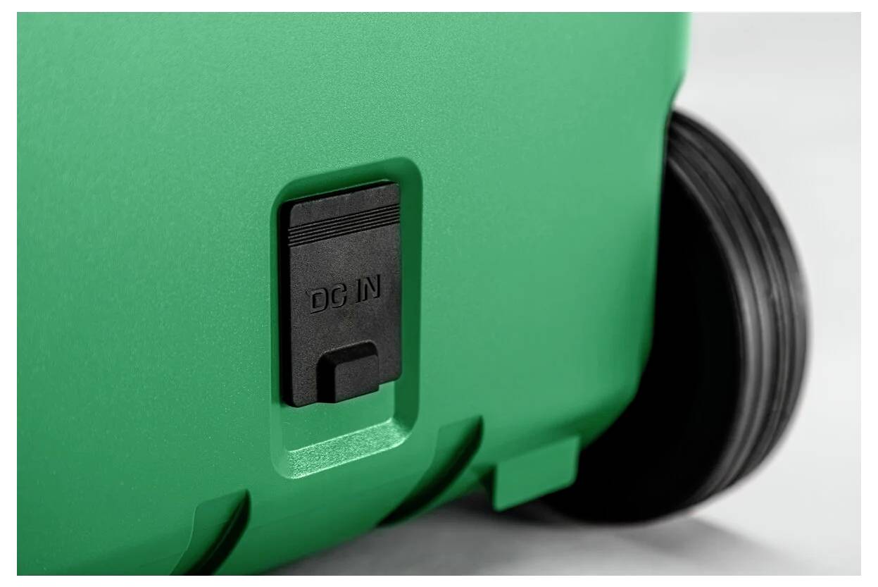 Close-up van een groen apparaat met een zwarte 'DC IN' stroomingangop en een wiel of roller aan de rechterkant.