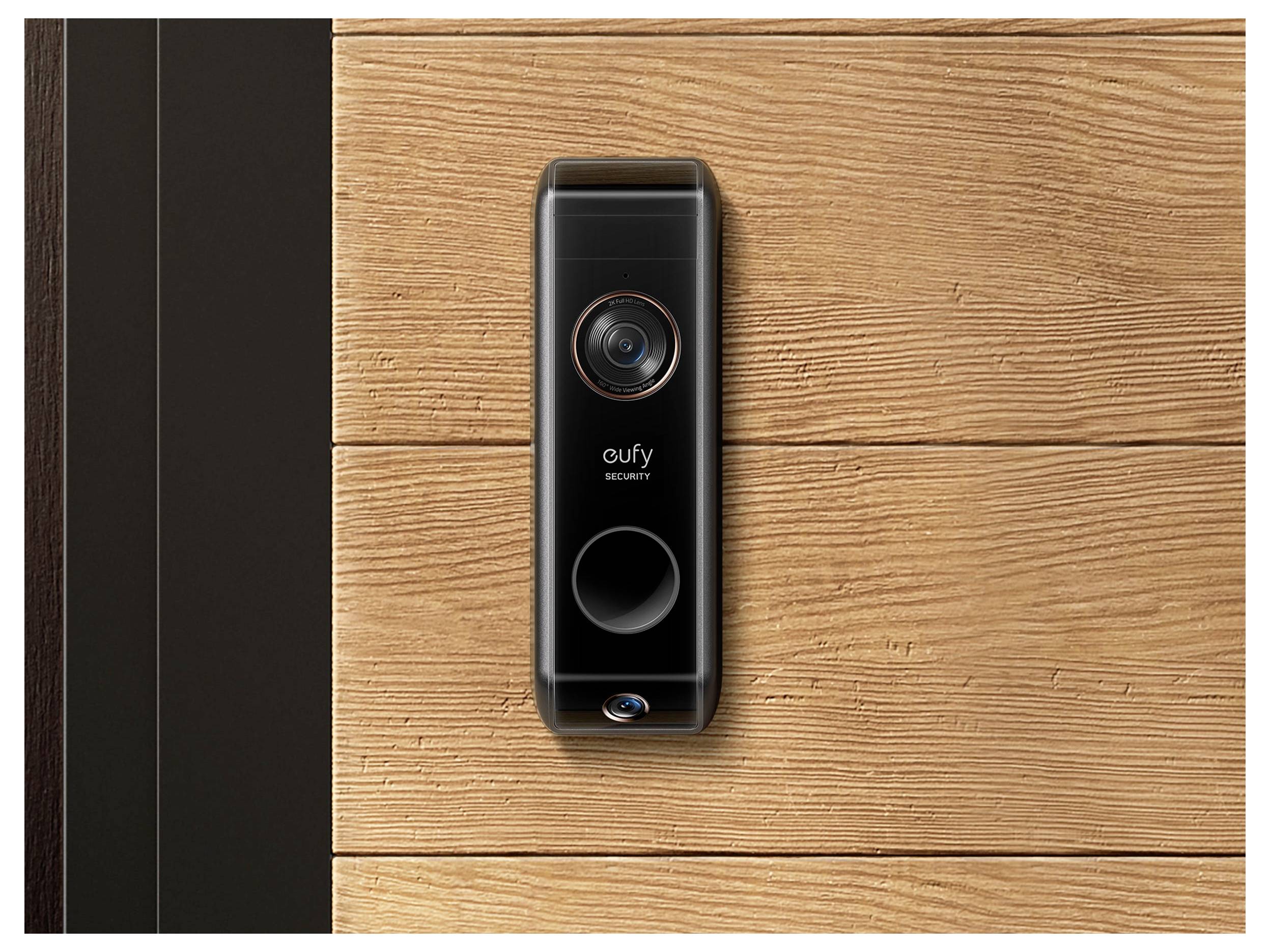 Zwarte eufy Security videodeurbel gemonteerd op een houten voordeur naast een donker deurkozijn.