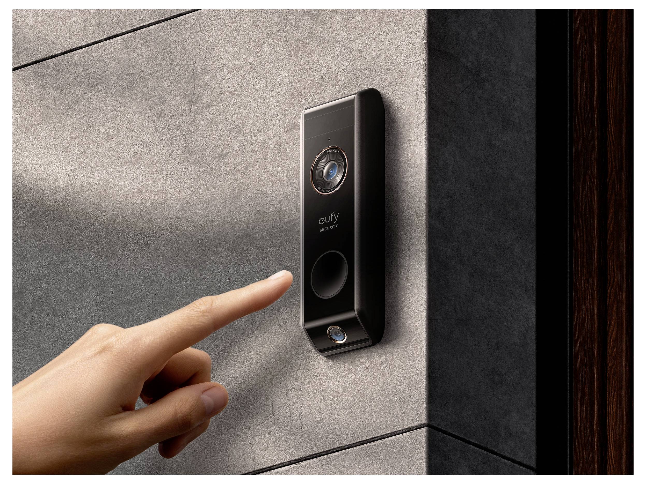 Een hand drukt op de knop van een aan de muur gemonteerde Eufy videodeurbel met cameralens.