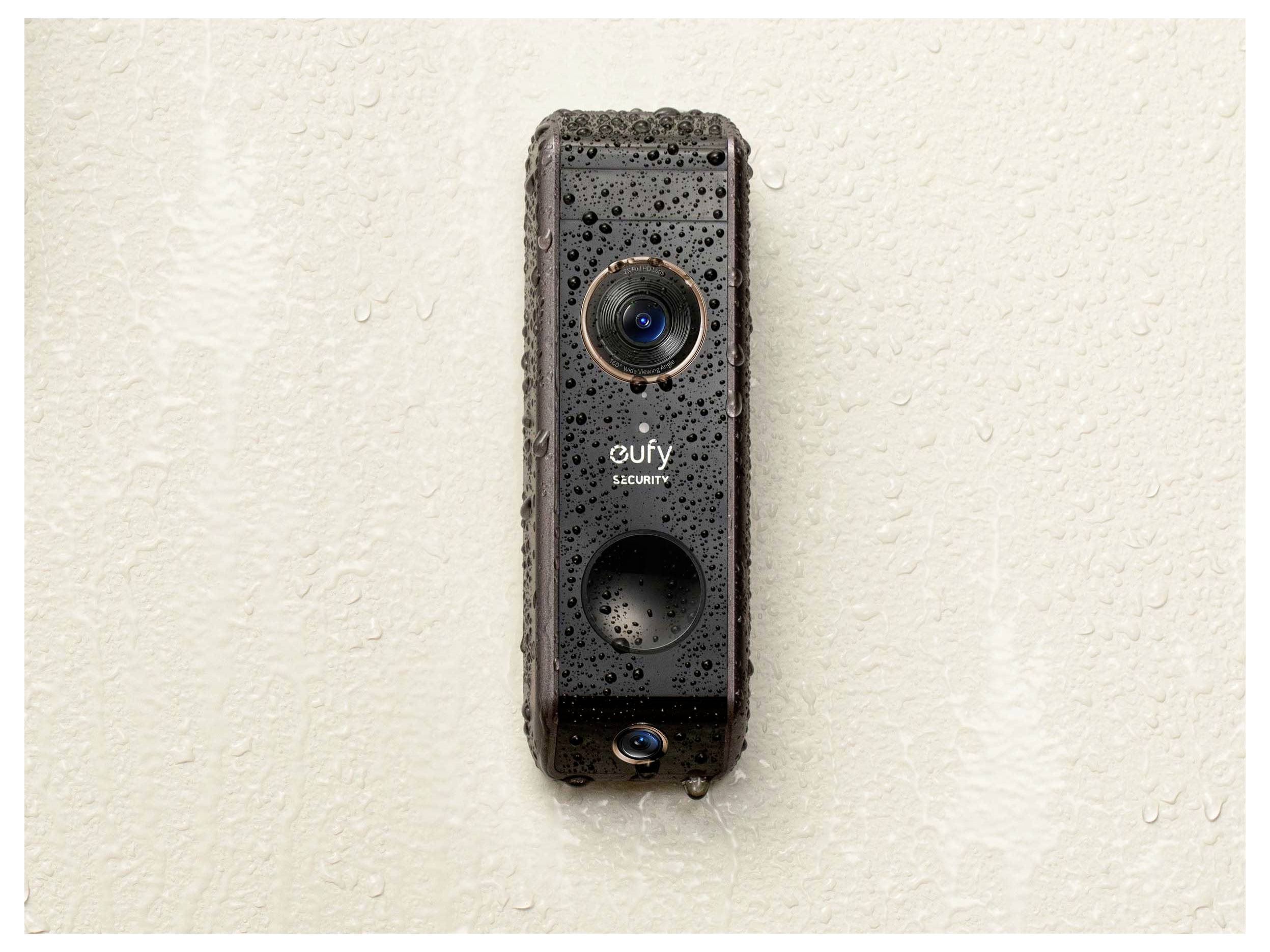 Een natte zwarte Eufy beveiligingsdeurklocamera gemonteerd op een lichte muur.