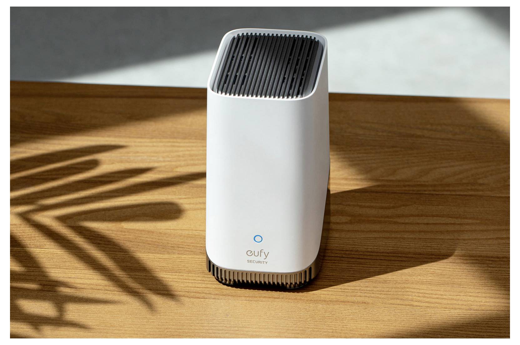 Wit Eufy Security-apparaat dat op een houten tafel in het zonlicht staat, met plantschaduwen ernaast geworpen.