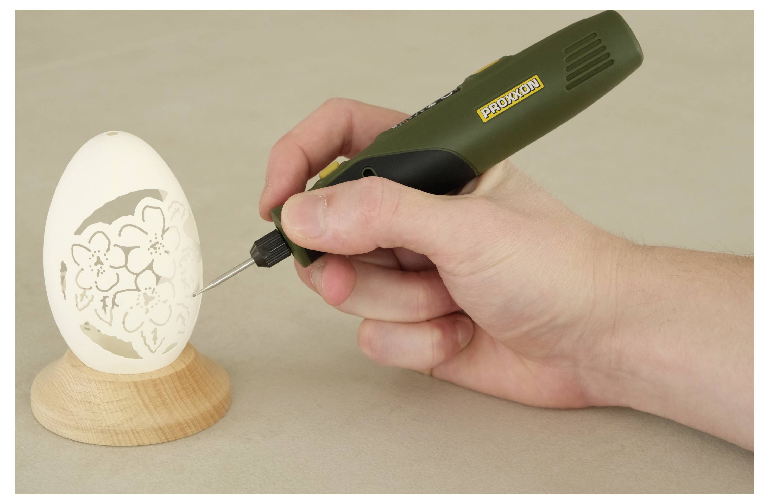 Een decoratief patroon met de hand in een wit ei op een houten standaard graveren met een penvormig graveergereedschap.