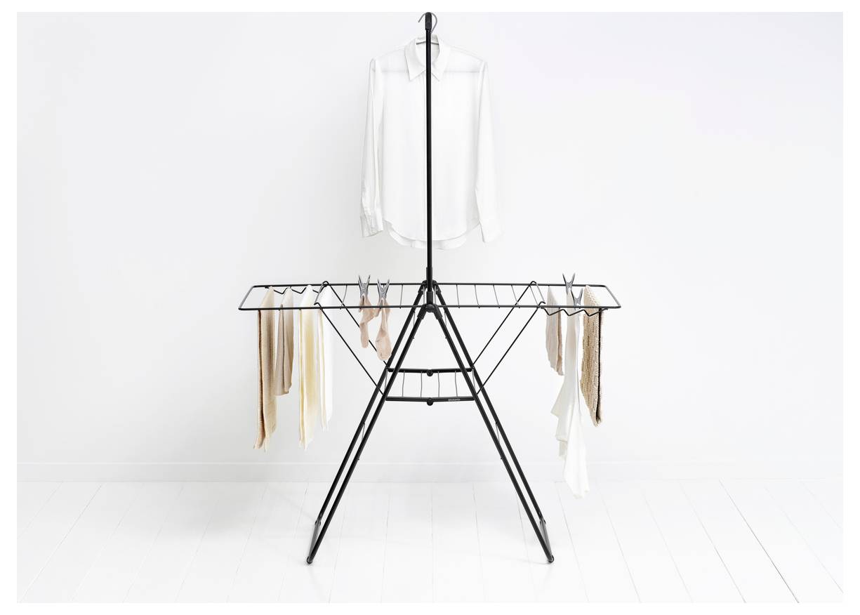 Minimalistische kledingrekdisplay met een witte blouse die erboven hangt en meerdere sjaals of kledingstukken die aan de zijkanten zijn gedrapeerd tegen een witte muur en vloer.