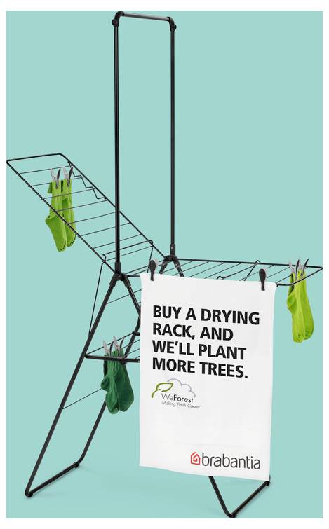 Promotiefoto van een droograck met wasgoed en een bord met de tekst 'KOO EEN DROOGRACK, EN WIJ PLANTEN MEER BOMEN.' met TreeForest- en Brabantia-logo's.