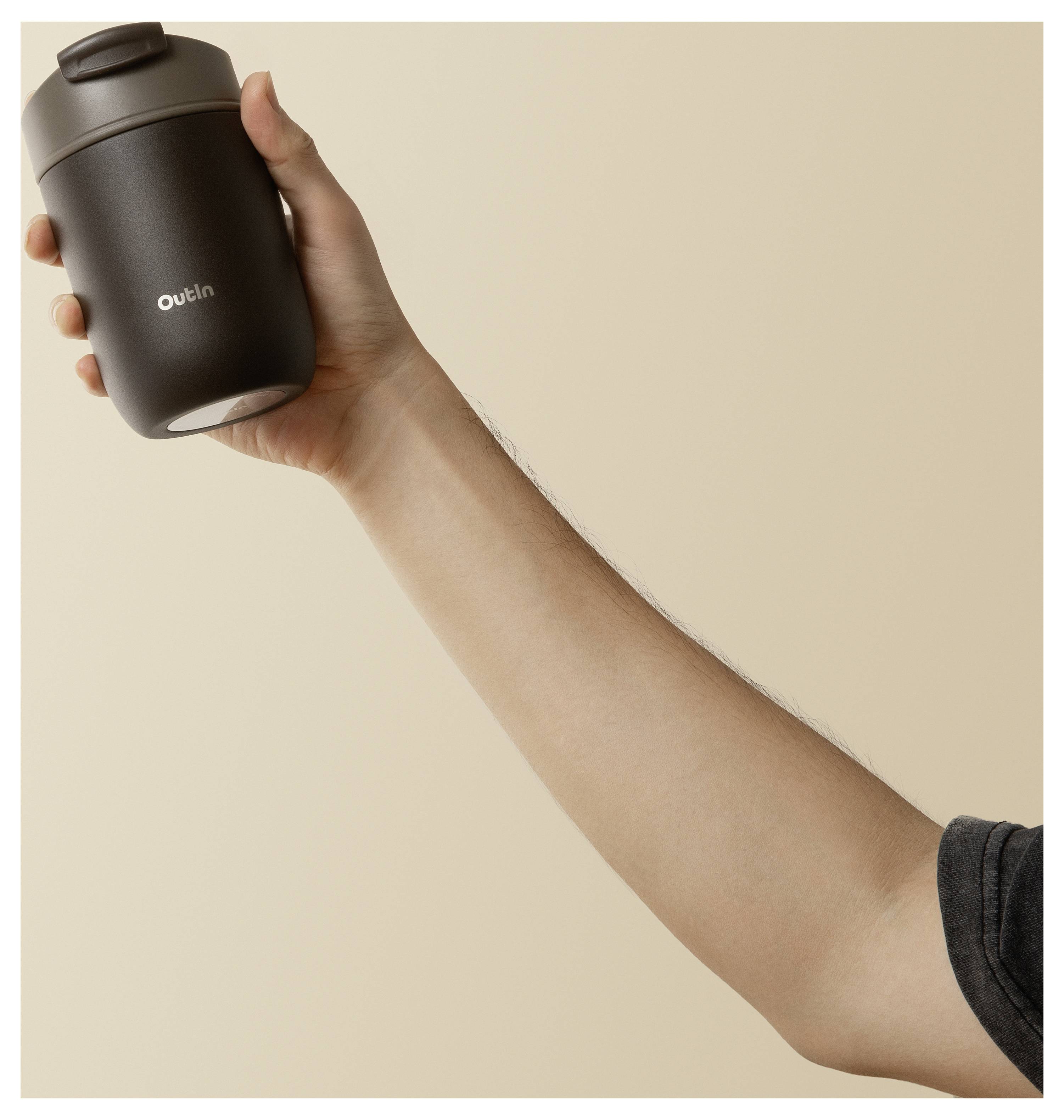 Hand die een matte zwarte reizigersbeker vasthoudt met het woord 'Outlin' tegen een effen beige achtergrond.