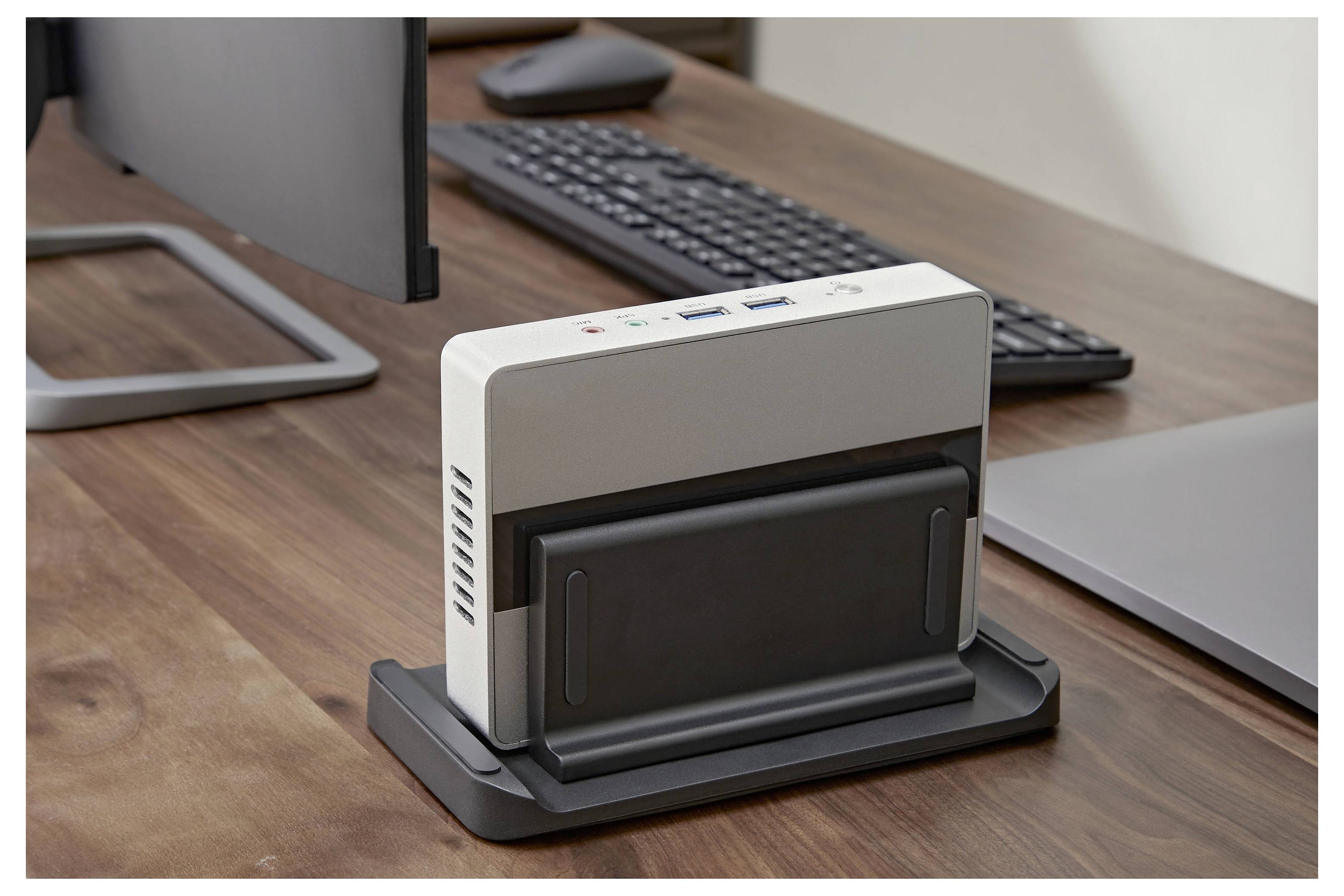 Een desktopelektronisch apparaat gekoppeld op een zwarte basis op een houten kantoorbureau, met monitor, toetsenbord en laptop op de achtergrond.