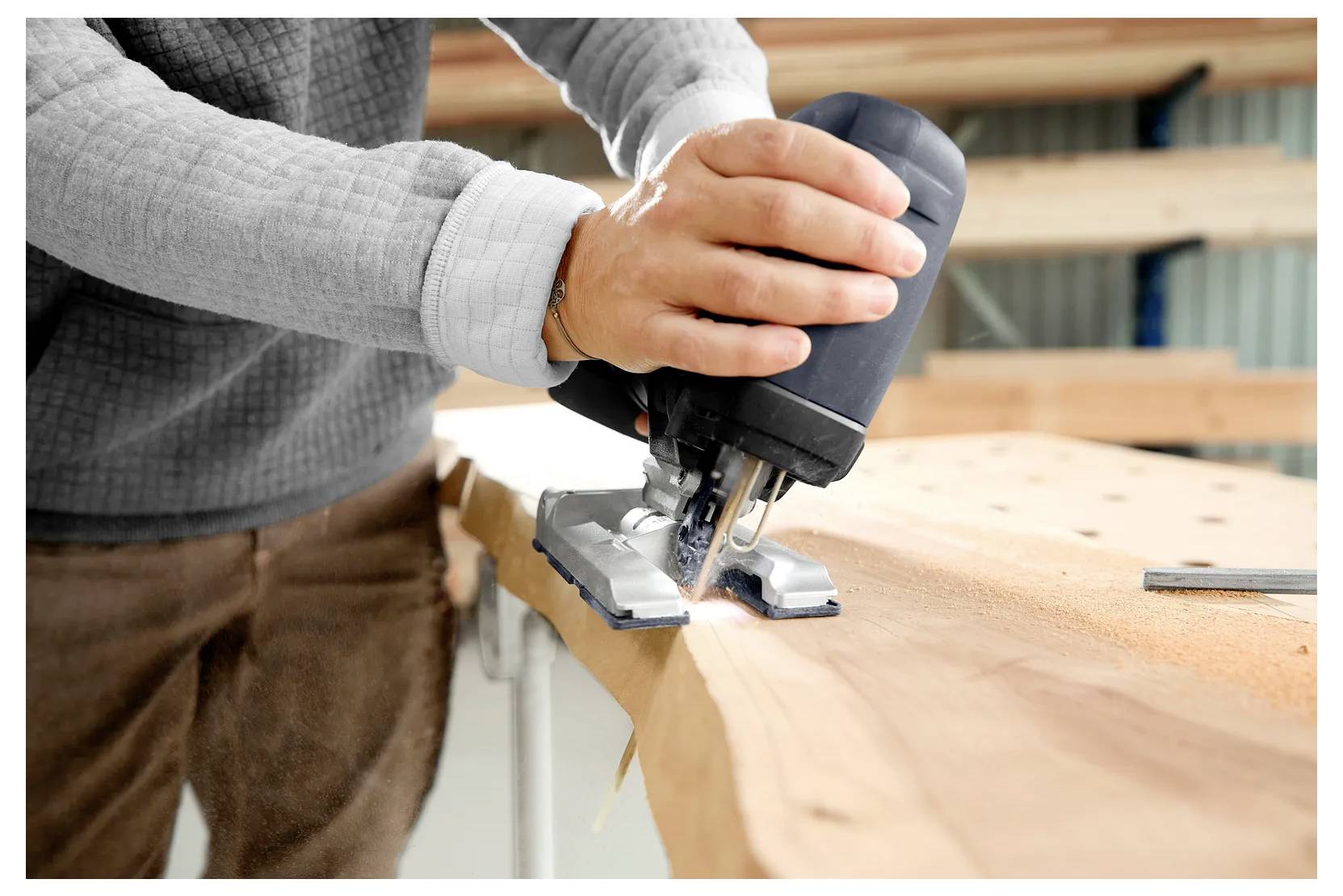 Zicht van dichtbij op een persoon die een decoupeerzaag gebruikt om een houten plank in een werkplaats te zagen.