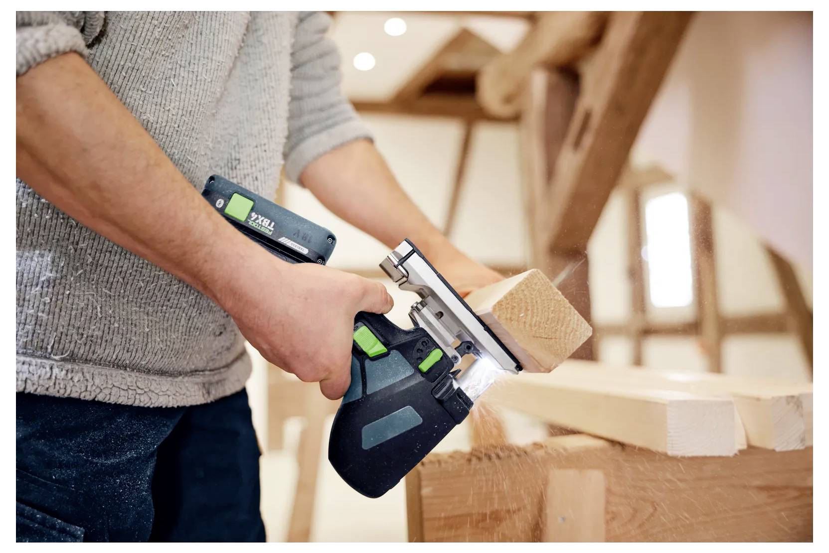 Persoon die een handheld elektrische schaafmachine gebruikt om een houten plank in een werkplaats glad te schaven, met houtsnippers die op de werkbank vallen.