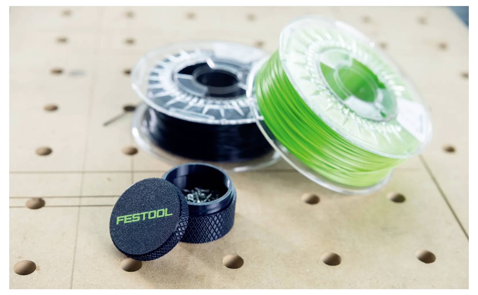 Drie spoelen met doorschijnend filament en een zwarte Festool-container staan op een geperforeerde werkbank.