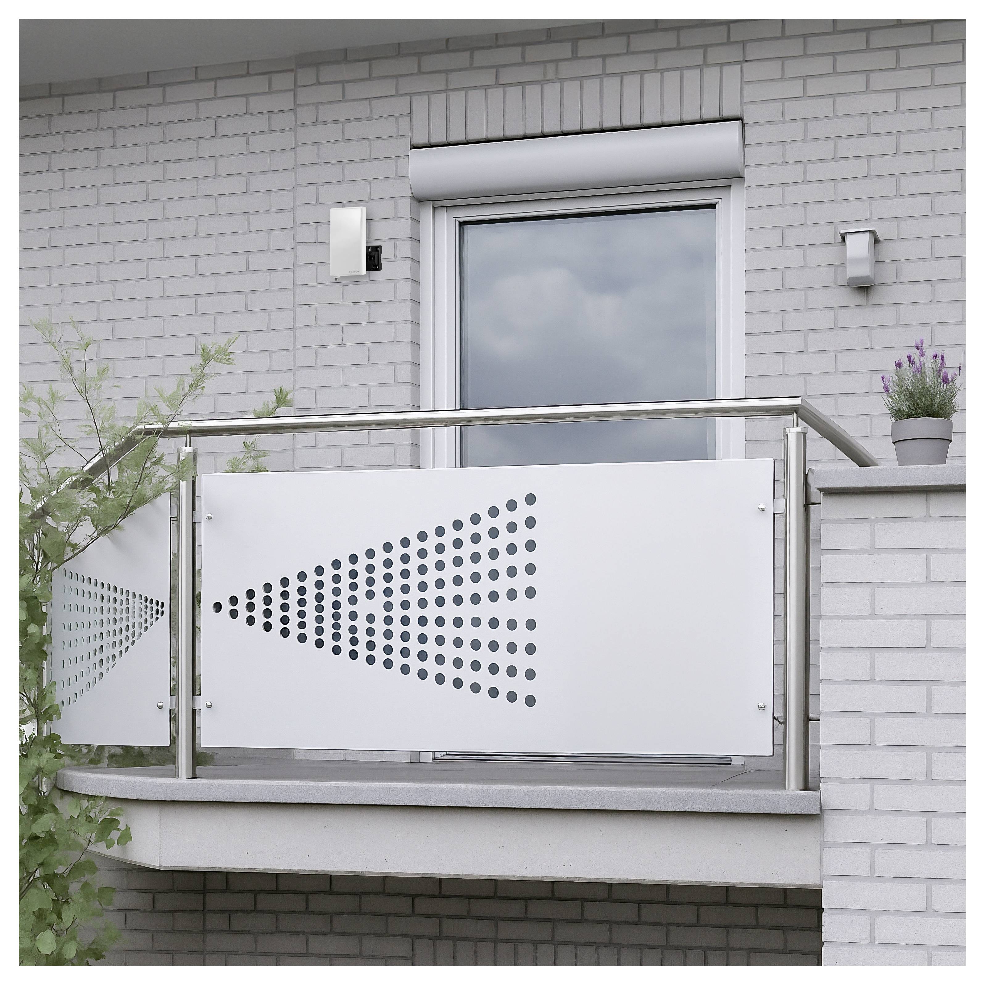 Modern balkon met witte geperforeerde metalen privacypanelen en een roestvrijstalen leuning tegen een grijzen baksteenmuur van een appartement, met een raam en een kleine potplant.