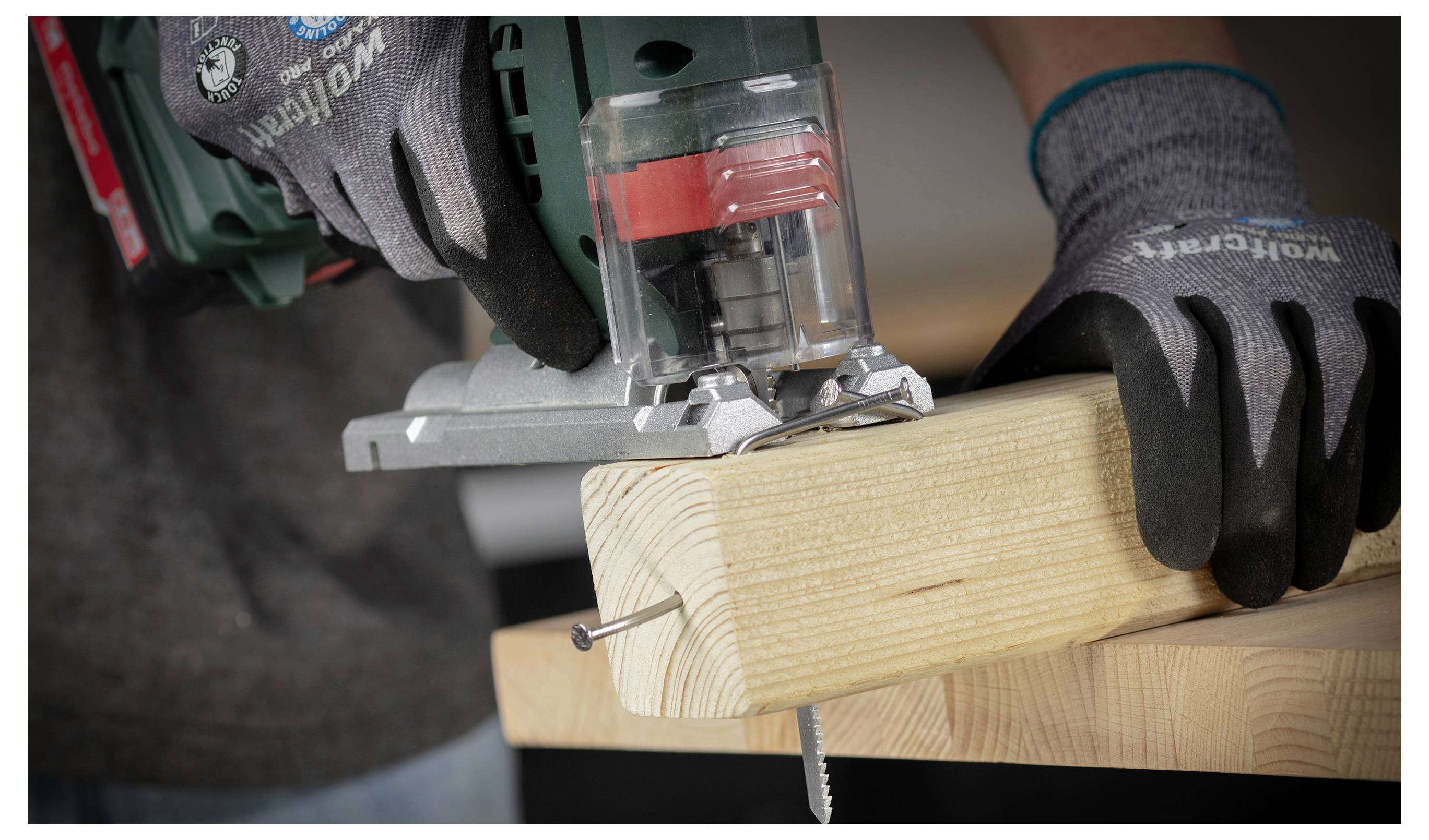 Handschoenen dragend handen die een elektische figuurzaag gebruiken om een houten plank door te zagen die met schroeven is ingeklemd in een werkplaats.
