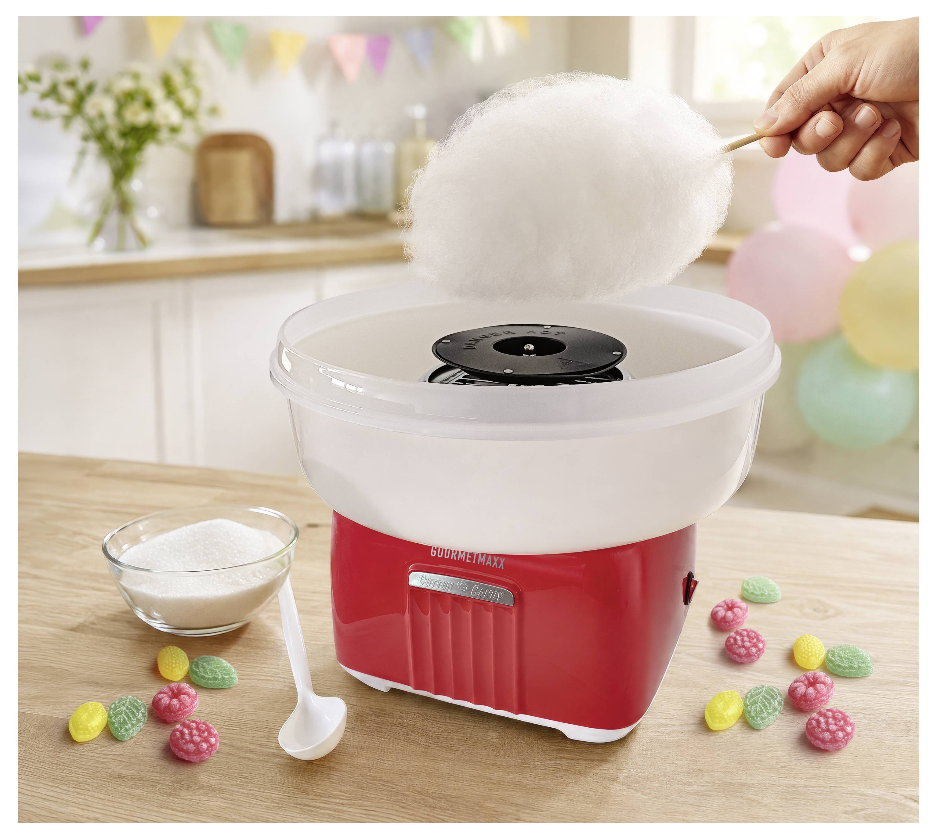 Een suikerspinmachine laat fluffy witte suikerspin op een stok draaien, met een suikerpot, lepel en gekleurde snoepjes op een tafel.