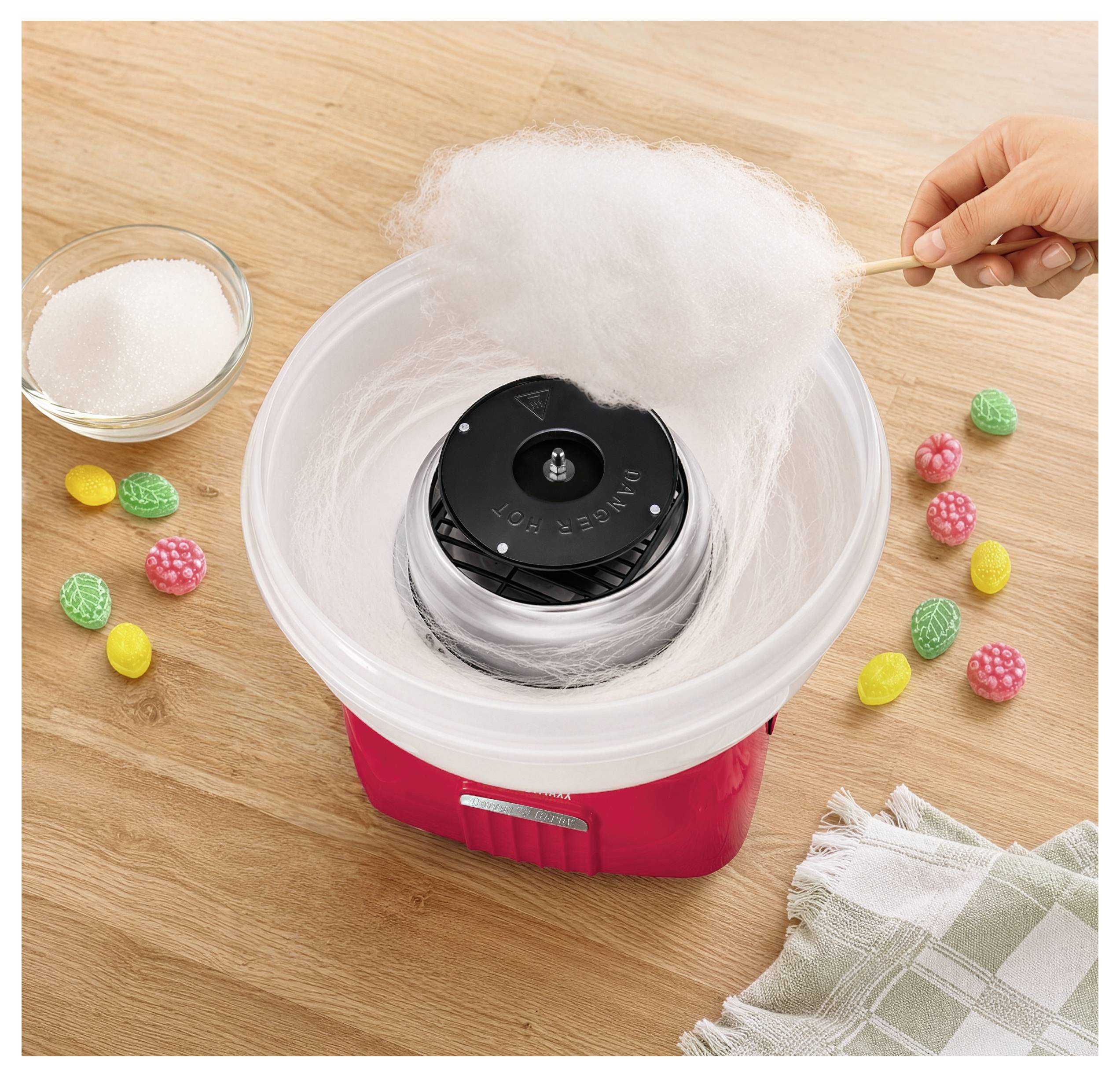Suikerspin machine die witte floss spinnen terwijl een hand suiker toevoegt; kom en gekleurde snoepjes op een houten tafel.