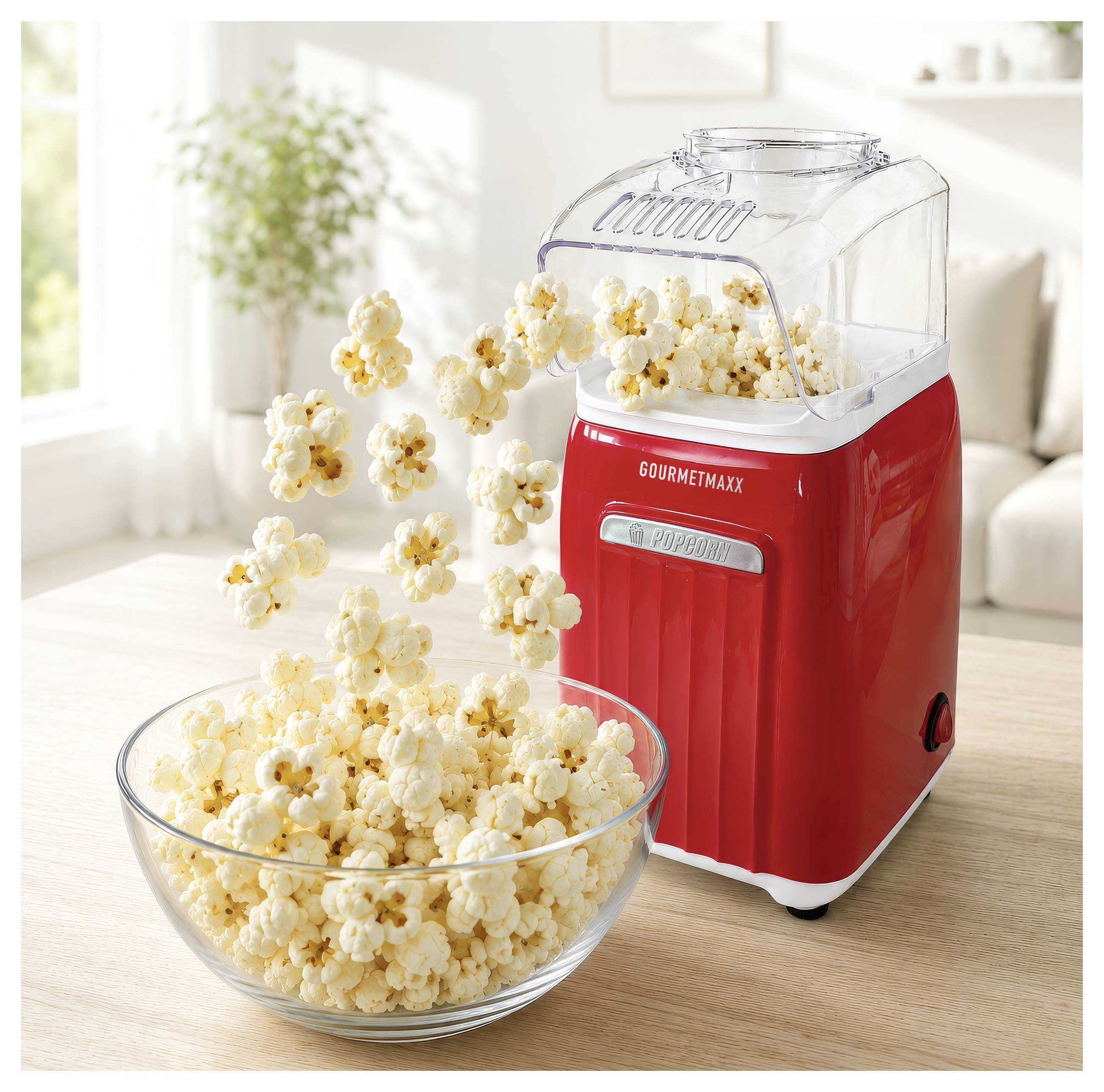 Rode popcornmachine die popcorn in een glazen kom op een tafel in een helder woonkamer uitgeeft.