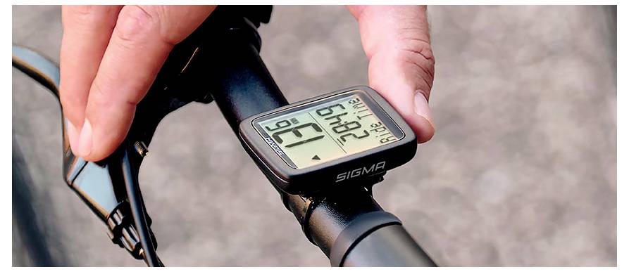 Close-up van een fietsstuur met een Sigma digitale fietscomputer die ritgegevens weergeeft terwijl een hand deze aanpast.