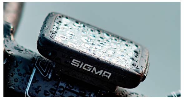 Close-up van een met regendruppels bespatten Sigma-fietslamp gemonteerd op een fietssstuur tegen een wazig tealblauw achtergrond.