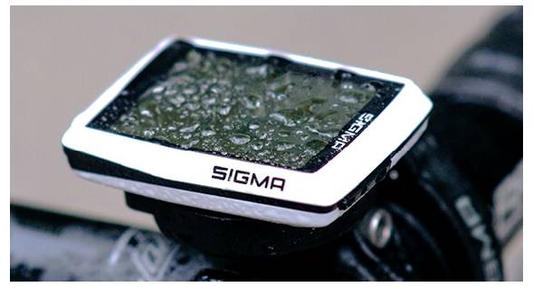 Close-up van een natte Sigma fietscomputer gemonteerd op het stuur, met regendruppels op het scherm.