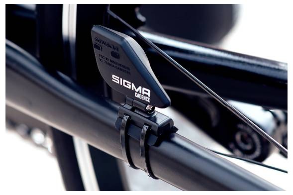 Close-up van een Sigma Cadence-sensor gemonteerd op een fietsenframe nabij de crank en ketting, gebruikt voor het meten van trapfrequentie.