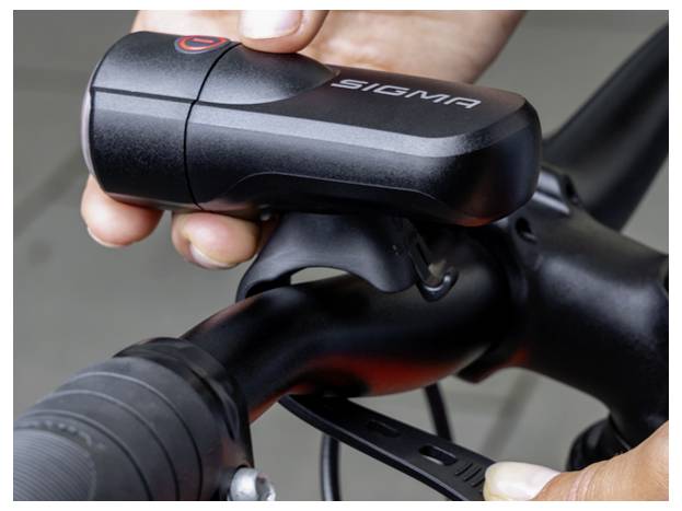 Close-up van een Sigma fietsvoorlicht dat op een fietsuur wordt gemonteerd met handen die de beugel aandraaien.
