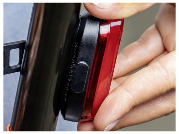 Close-up van een persoon die een rood fietstaachlicht aan de zadelpen bevestigt.